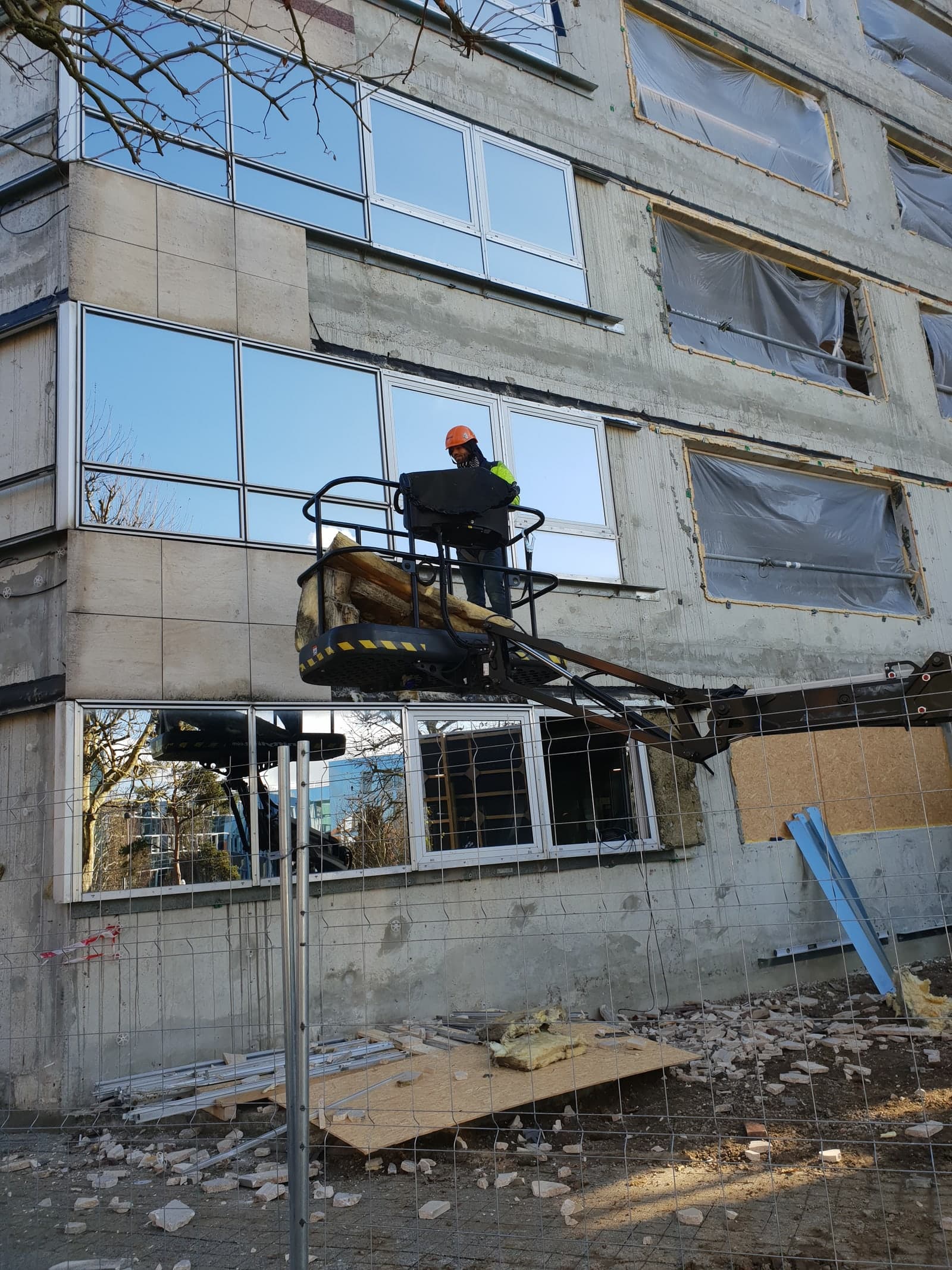 Compagnon IEF en nacelle ciseaux posant une menuiserie en façade
